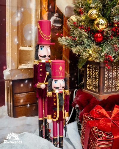Deux casse-noisettes devant un sapin décoré et un cadeau à ruban rouge.